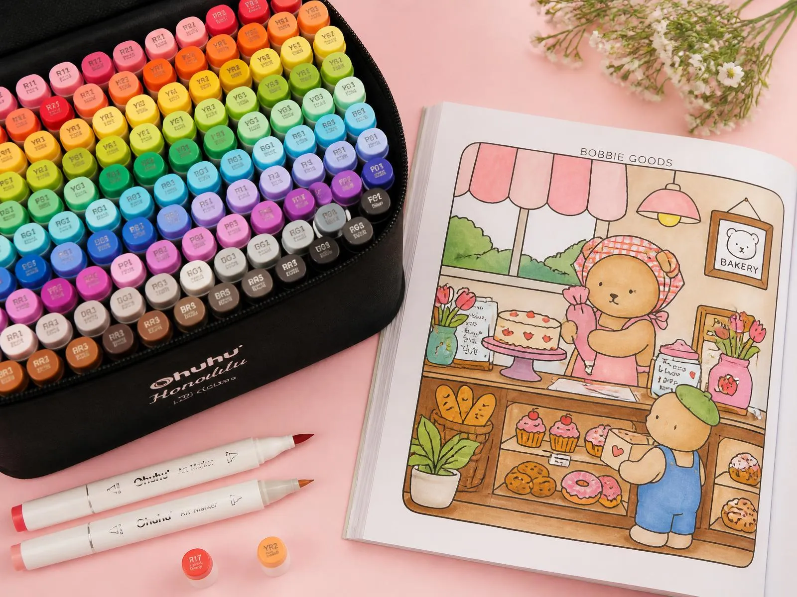 Diversos marcadores e canetinhas coloridas ao lado de uma página de desenho fofo estilo Bobbie Goods sendo colorida